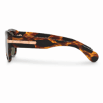 Lentes de sol Gucci con montura carey en vista lateral, cristales oscuros y detalle metálico con logo sobre fondo blanco.