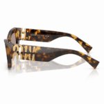Lentes de sol Miu Miu en vista lateral, con montura carey, patillas anchas y logo dorado Miu Miu sobre fondo blanco.