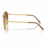 Lentes de sol Ray-Ban en vista lateral, con varillas doradas grabadas, terminales beige y cristales marrón degradado sobre fondo blanco.